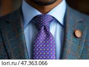 A close-up of a man's suit, emphasizing the details of a business style. In the center is a bright purple tie with a pattern of turquoise-green and orange circles. The tie is tied in a neat knot. The shirt is light blue with a thin stripe, and the jacket is made of fabric with a pronounced texture - a dark background with small blue specks and a brown check. A round embossed badge is attached to the lapel of the jacket. The entire composition conveys a sense of sophisticated style, individuality and an attentive approach to detail. Стоковое AI-изображение, AI-художник Анна Кривицкая / Фотобанк Лори
