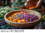 A scene from the world of aromatherapy and herbalism. In the center of the frame is a wooden bowl filled with brightly colored dried petals of various colors: yellow, purple, pink, blue and orange. Someone's hand carefully pours essential oil or tincture from an amber glass bottle directly onto the flower mixture. Fresh and dried herbs also lie around the bowl, creating an atmosphere of natural comfort, healing and peace of mind. The entire image is filled with aromas, warmth and a sense of care for the body and spirit. Стоковое AI-изображение, AI-художник Анна Кривицкая / Фотобанк Лори