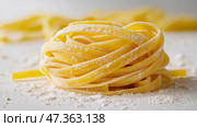 Fresh Fettuccine Pasta Bundle. Minimalist Food Photography. Аккуратная золотистая пачка свежеприготовленных макарон фетучине со слегка припорошенной мукой текстурой на бесшовном белом фоне. Мягкие изгибы макарон создают нежную, органичную композицию. Стоковое AI-изображение, AI-художник Katsiaryna Repich / Фотобанк Лори