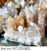 A spectacular group of quartz crystals growing out of a common rock. The crystals have different colors: from transparent and white to light orange and pale pink. They shine, reflecting light from the edges, which emphasizes their natural purity and geometric shape. The minerals are carefully arranged on the stone substrate, creating the feeling of natural growth. Стоковое AI-изображение, AI-художник Анна Кривицкая / Фотобанк Лори