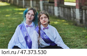 Two happy graduates celebrating their last school day, sitting on the grass in the schoolyard, wearing sashes and enjoying the moment as friends and classmates. Стоковое фото, фотограф Mikhail Davidovich / Фотобанк Лори