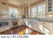 A bright and cozy kitchen in a classic style with modern elements. The spacious room is illuminated by natural light through large windows. The kitchen set is made in white, with granite countertops and a backsplash made of white glossy tiles. The center of attention is a large farmhouse-style sink, built-in stainless steel appliances (oven, microwave, dishwasher), wooden flooring adds warmth and coziness. The image of an ideal family kitchen. Стоковое AI-изображение, AI-художник Анна Кривицкая / Фотобанк Лори