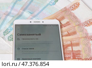 Смартфон с открытым банковским приложением -  личным кабинетом самозанятого (плательщиков налога на профессиональный доход) на фоне пятитысячных и тысячных  купюр. Стоковое фото, фотограф Snezka / Фотобанк Лори