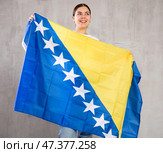 Joyous young woman holding Bosnia flag against unicoloured background. Стоковое фото, фотограф Яков Филимонов / Фотобанк Лори