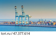 Manama, Bahrain - Jan 08 2024, Panoramic view of Bahrain commercial port with blue cranes, buildings and containers, with sea on foreground, by the morning, dawn, sunrise, Manama, Bahrain. Редакционное фото, фотограф Сергей Богомяко / Фотобанк Лори