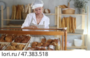 Woman employee puts croissants in window, arranges display of goods at bakery. Стоковое видео, видеограф Яков Филимонов / Фотобанк Лори