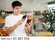 Male buyer checks suitability - scans QR code on jar of ketchup label in grocery store. Стоковое фото, фотограф Яков Филимонов / Фотобанк Лори