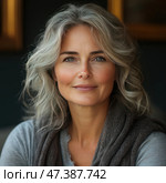 Portrait of a mature woman with grey wavy hair and a clear, confident look. Her face radiates calm, warmth and inner strength. She is dressed in a grey sweater and a warm scarf, and the background is softly darkened, creating an atmosphere of coziness and depth. Soft lighting emphasizes the natural beauty, wrinkles and texture of the skin, not hiding age, but on the contrary - emphasizing dignity and harmony. Стоковое AI-изображение, AI-художник Анна Кривицкая / Фотобанк Лори