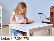 Young Girl Using Tablet at Table with Focused Expression. Стоковое фото, фотограф Кутина Татьяна / Фотобанк Лори
