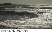 A dramatic scene of the ocean with waves shimmering under the light. The silhouette of a pier or dock is visible in the foreground, and the horizon is slightly obscured by the rough sea. Стоковое видео, видеограф Воловодов Владимир / Фотобанк Лори