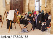 Manama, Bahrain - Jan 15 2024, An Arab woman dressed in a black burqa and niqab enthusiastically tells group of tourists about history of Islam inside of the Grand Mosque Al Fateh, Manama, Bahrain. Редакционное фото, фотограф Сергей Богомяко / Фотобанк Лори
