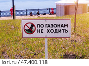 Табличка По газонам не ходить с изображением ноги в красном перечеркнутом круге на фоне набережной и отдыхающих спортсменов (2024 год). Стоковое фото, фотограф Евгения Золкина / Фотобанк Лори