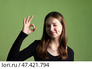 Teen Girl Expresses Confidence With a Playful Gesture Against a Green Background in a Studio Setting. Стоковое фото, фотограф Aleksandr Golubev / Фотобанк Лори