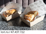 Сэндвичи с вкусным свежим хлебом с хрустящей корочкой и начинками в оберточной бумаге и картонном одноразовом лотке, купленный на фудкорте, крупным планом. Стоковое фото, фотограф Татьяна Васильева / Фотобанк Лори