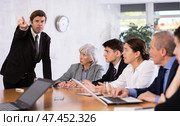 Furious male boss yelling at office colleagues of different ages taking notes at table with laptops. Стоковое фото, фотограф Яков Филимонов / Фотобанк Лори