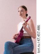 Woman musician strumming ukulele and looking away. Talented woman plucking with blank expression. Стоковое фото, фотограф А. А. Пирагис / Фотобанк Лори