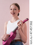 Happy musician woman is very lovely as she smilingly plays ukulele and friendly looking at camera. Стоковое фото, фотограф А. А. Пирагис / Фотобанк Лори