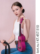 Female musician sitting and holding ukulele vertically, looking camera with blank expression on face. Стоковое фото, фотограф А. А. Пирагис / Фотобанк Лори