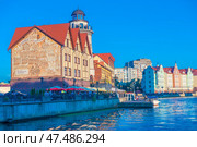 One of the most recognizable tourist sites in Kaliningrad is the Fish Village. This is a stylized architectural complex on the embankment of the Pregolya River. The buildings are decorated in the spirit of German half-timbered houses, the facade of one of the houses is decorated with a large mural with historical scenes. In the foreground are pleasure boats, street cafes with bright umbrellas and tourists relaxing. The atmosphere of a warm summer evening is emphasized by soft light and a bright blue sky. (2020 год). Редакционное фото, фотограф Анна Кривицкая / Фотобанк Лори