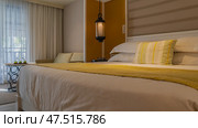 A double bed with white sheets and a yellow bedspread. Pillows at the headboard. The lamp is lit. There is a sofa in the corner by the window. There are green apples and glasses on the coffee table. Стоковое фото, фотограф Вера Ивановна Кубарева / Фотобанк Лори
