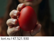 Женщина держит красное пасхальное яйцо на вытянутой руке. Стоковое AI-изображение, AI-художник Анна Рогалева / Фотобанк Лори
