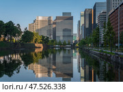 Tokyo, Japan, 11.04.2024: Skyscrapers of the Marunouchi business district in Chiyoda Ward with reflection in the Babasaki moat of the Tokyo Imperial Palace on a sunny day. Редакционное фото, фотограф Ula Ulachka / Фотобанк Лори
