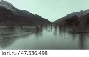 Aerial - Turquoise alpine reservoir mirroring bare trees, snow capped Pyrenees peaks surrounding tranquil Ibon de los Banos landscape in Huesca, Spain. Стоковое видео, видеограф Данил Руденко / Фотобанк Лори