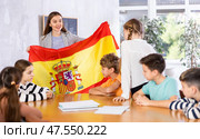 Excited female teacher discussing with preteens students state flag of Spain in auditory of middle school. Стоковое фото, фотограф Яков Филимонов / Фотобанк Лори