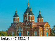 Majestic Orthodox church - Iverskaya Church, located in the village of Borshchevoe, Venevsky district. The building is made of red brick and decorated with white decorative elements. The temple has several high octagonal domes with golden crosses, covered with a dark roof. The central entrance stands out with a bright blue door, and a wide staircase leads to it. The architecture is distinguished by harmonious proportions and classical Russian church style. In the background is a clear blue sky, emphasizing the monumentality of the building. Стоковое фото, фотограф Анна Кривицкая / Фотобанк Лори