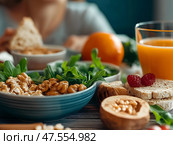 Healthy breakfast with walnuts, greens, bread and orange juice on rustic table, nutrition concept, AI. Стоковое AI-изображение, AI-художник Raquel Corcoles Mendez / Фотобанк Лори