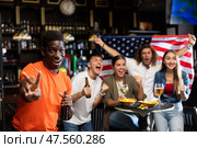 Happy multiracial sport fans holding the flag of USA, enjoing game, beer and chips in the bar. Стоковое фото, фотограф Яков Филимонов / Фотобанк Лори