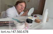A beautiful senior woman is sitting at home and doing her make-up morning routine. Senior woman putting blush on her face. Стоковое видео, видеограф Ирина Старикова / Фотобанк Лори