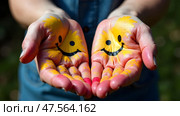 Two open hands with painted smiley faces and colorful splashes, held out against a blurred background. Concept of happiness, creativity, and positivist. Стоковое AI-изображение, AI-художник Александра Рублева / Фотобанк Лори
