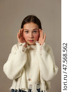 Teen Girl Expressing Curiosity While Posing in a Cozy Sweater Against a Neutral Backdrop. Стоковое фото, фотограф Aleksandr Golubev / Фотобанк Лори