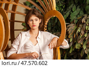 Teen Girl in a Stylish Chair Surrounded by Lush Greenery Expresses Thoughtful Contemplation. Стоковое фото, фотограф Aleksandr Golubev / Фотобанк Лори