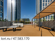 Bright outdoor space features modern seating and landscaping, nestled between tall buildings. Sunlight enhances the inviting atmosphere, perfect for gatherings or relaxation. Стоковое фото, фотограф Алексей Климкин / Фотобанк Лори