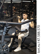 In gym, man uses lat pulldowm machine to strengthen arm muscles. Стоковое фото, фотограф Яков Филимонов / Фотобанк Лори