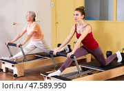 Elderly woman and young girl practicing on Pilates reformer. Стоковое фото, фотограф Яков Филимонов / Фотобанк Лори