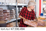 Elderly woman buys briquettes with red clay in specialized store. Стоковое фото, фотограф Яков Филимонов / Фотобанк Лори