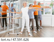 Mature woman in sportswear participating 2nd position of ballet stance at barre with group in choreography studio. Стоковое фото, фотограф Яков Филимонов / Фотобанк Лори