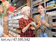 Two women consult with each other what pigment or acrylic varnish to choose for their future clay or ceramic dishes in specialized store. Стоковое фото, фотограф Яков Филимонов / Фотобанк Лори