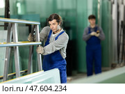 Man glazer employee in blue overall works in glass processing shop. Стоковое фото, фотограф Яков Филимонов / Фотобанк Лори