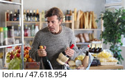 Casual middle-aged man thoughtfully comparing two wine bottles, examining labels and pondering choice with focused expression while shopping in grocery store. Стоковое видео, видеограф Яков Филимонов / Фотобанк Лори