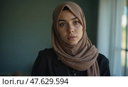 Young Muslim Woman in Hijab Sits Indoors, Staring at the Camera With a Troubled Expression. Стоковое AI-изображение, AI-художник Sergey Grishin / Фотобанк Лори