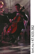 A cellist in a tuxedo passionately plays the instrument as part of the orchestra on stage. Dim lighting and smoke on the stage. Concert of classical music. Russia, January 1, 2025. Редакционное видео, видеограф Воловодов Владимир / Фотобанк Лори