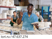 Positive man potter with new crafted crockry in workshop. Стоковое фото, фотограф Яков Филимонов / Фотобанк Лори