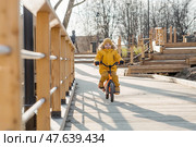 A cute boy in bright yellow clothes rides a bike. A happy child plays outside in early spring. Happy childhood. Стоковое фото, фотограф Photojuli / Фотобанк Лори