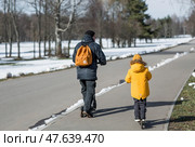 A little boy in bright yellow clothes and his dad ride scooters. A happy child and father are walking outside in early spring. Happy childhood and family. Стоковое фото, фотограф Photojuli / Фотобанк Лори