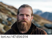 Male portrait in scenic terrain of mountains, forests in the winter. Bearded mature stylish hipster man. Active traveler hiker enjoying his retirement in the nature. Hiking in nature for wellness. Стоковое AI-изображение, AI-художник Марина Демидюк / Фотобанк Лори