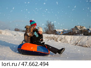On a winter day, children go sledding and laugh merrily. A boy and a girl go down the mountain on a sled. Children in the winter in the village on vacation. Стоковое фото, фотограф Лазаренко Светлана / Фотобанк Лори